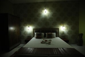 A dimly lit bedroom with a large bed, two bedside tables, and a wardrobe.