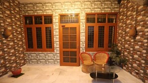 A stone-walled room with three wooden-framed windows, a glass table, and wicker chairs.