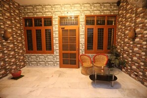 A stone-walled room with two wooden doors, a glass table, and wicker chairs. - Karta-Purakh an Ayurvedic Stay (Amritsar)