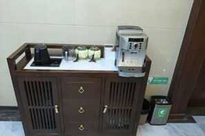 Una estación de café con cafetera, tazas y recipientes para condimentos.