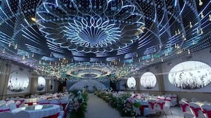 Un salón de banquetes con mesas redondas, sillas blancas y centros de mesa florales.