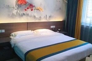 Una habitación de hotel con cama, mesita de noche, lámpara de pared y ventana con cortinas.