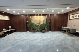 A modern hotel lobby with a marble floor, wooden paneling, a reception desk, seating area, and potted plants.