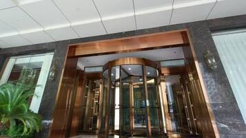 A hotel lobby with a revolving door, a potted plant, and a patterned carpet.