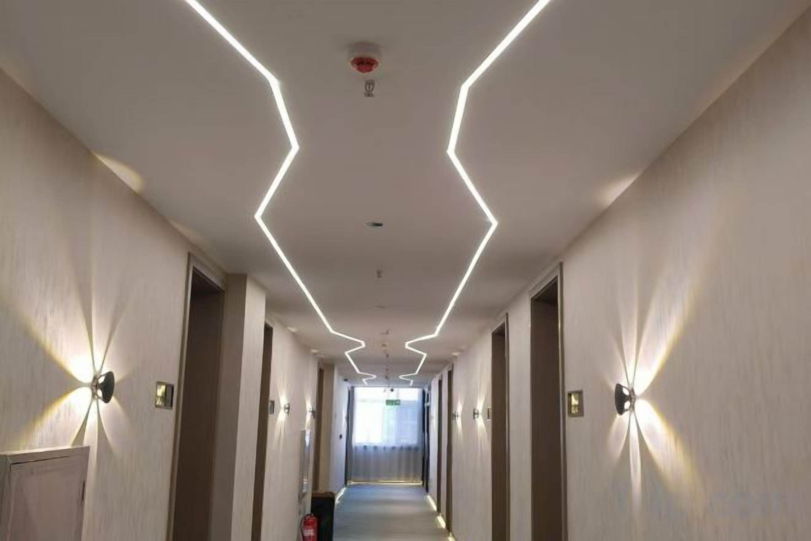 Un pasillo de hotel con diseño moderno, que presenta un camino recto, luminarias en las paredes y una señal de salida visible.