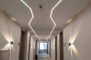 A hotel corridor with a modern design, featuring a straight path, light fixtures on the walls, and a visible exit sign. - Yue Cheng Commercial Hotel (Anping)
