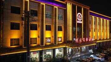 A hotel with multiple floors, a prominent entrance, and a parking area with several cars.