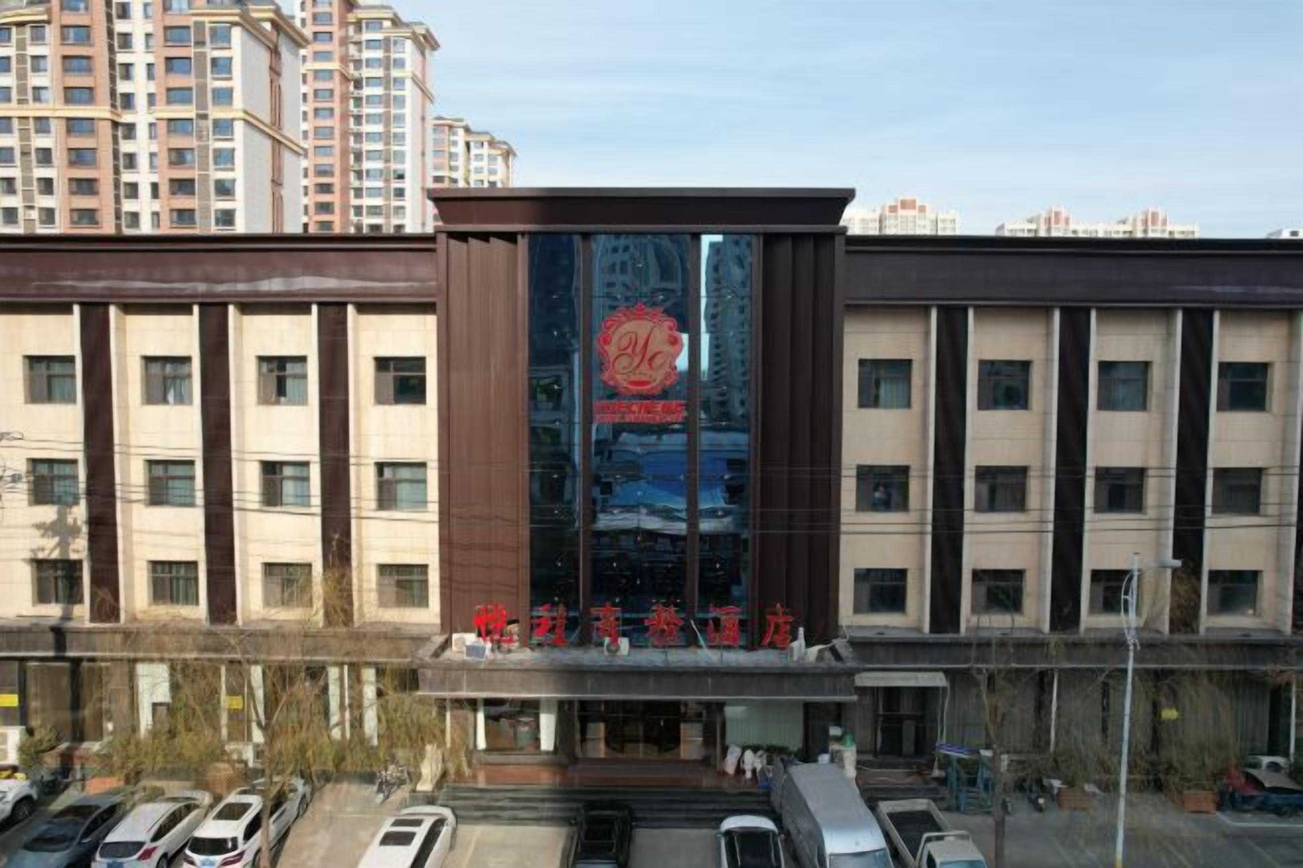 A hotel with a modern facade, a large glass entrance, and a parking lot with several cars.