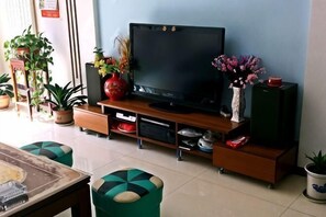 Un soggiorno con televisore a schermo piatto, mobile TV in legno, pouf verdi e piante in vaso.
