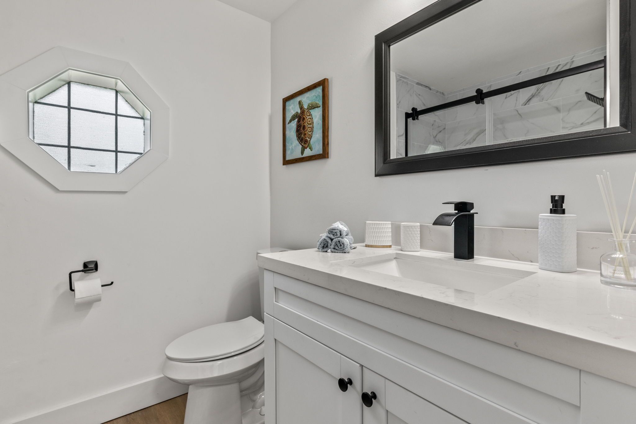 A modern bathroom with a white toilet, a white sink with a marble countertop, a large mirror, and a window with a geometric design.