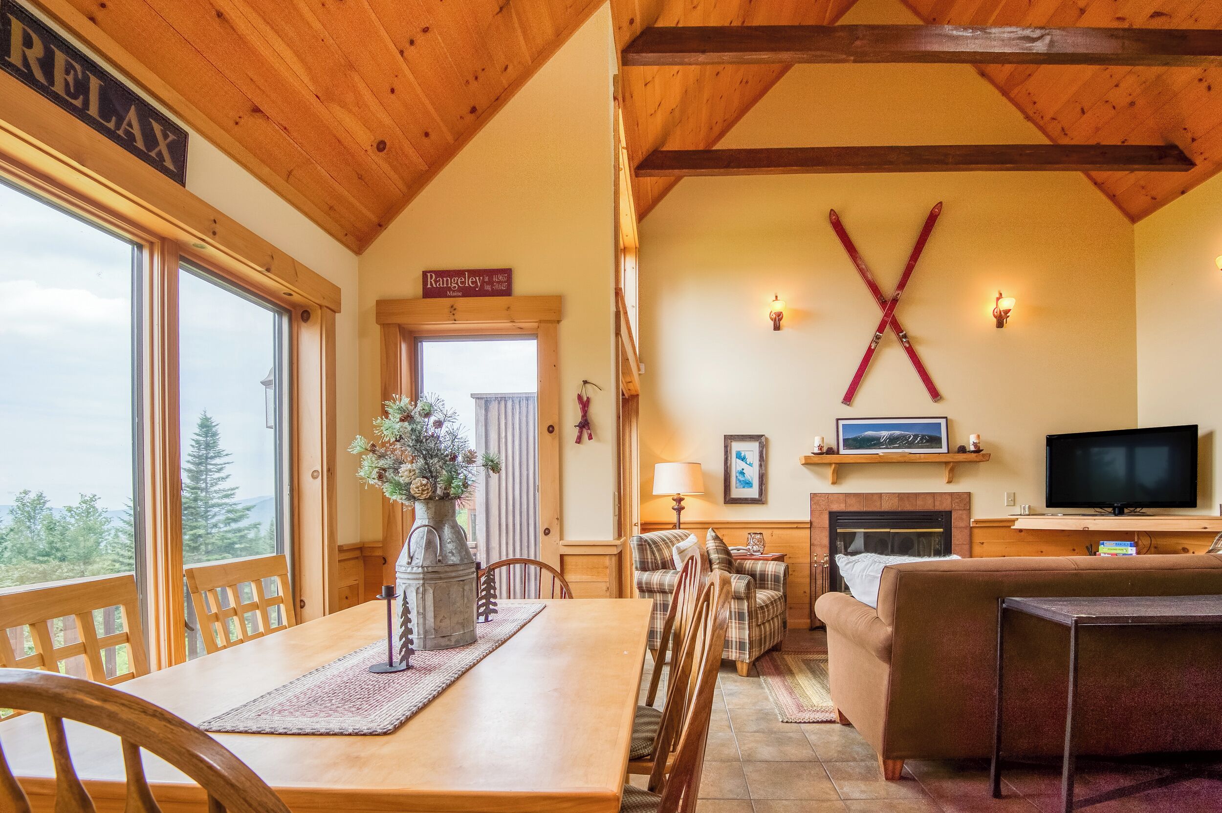 A cozy living room with a fireplace, a television, and a large window overlooking a forest.