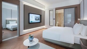 Una habitación de hotel moderna con una cama grande, un televisor montado en la pared y una pequeña mesa redonda con un jarrón.