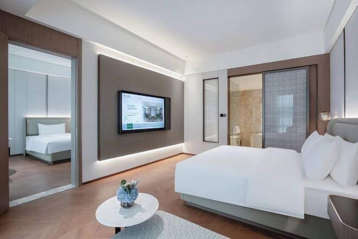Ein modernes Hotelzimmer mit einem großen Bett, einem an der Wand befestigten Fernseher und einem kleinen runden Tisch mit einer Vase.