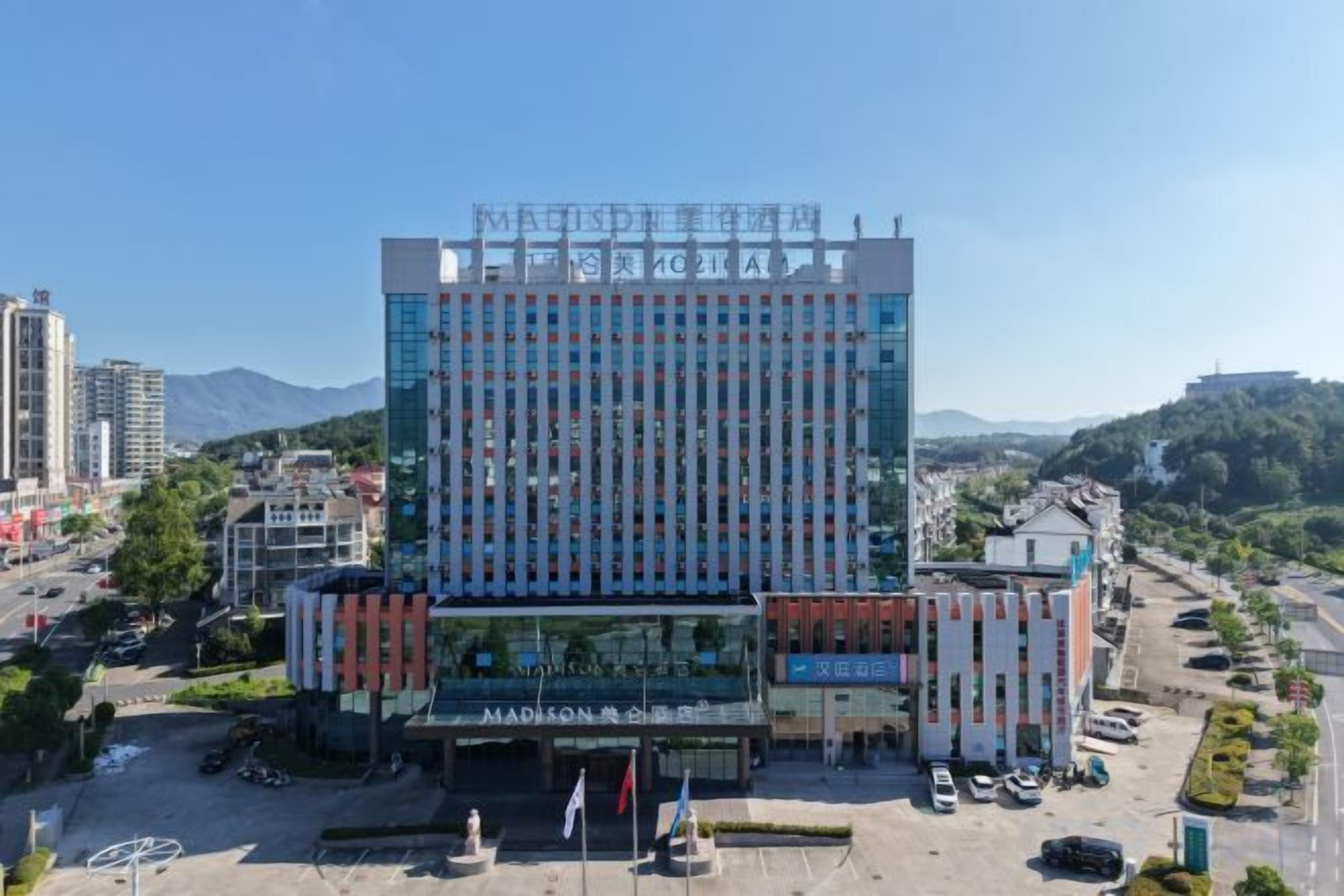 A multi-story building with a modern architectural design, featuring a prominent entrance with a glass facade and a flagpole.