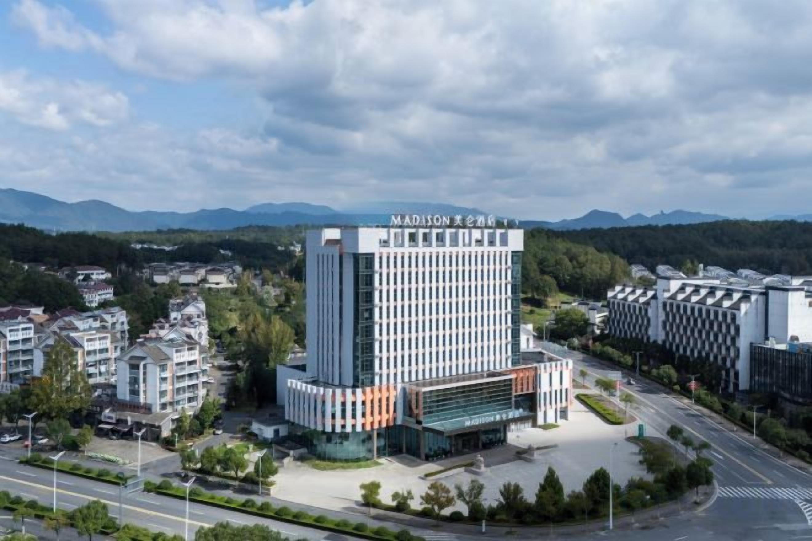 A modern hotel with a prominent central tower, surrounded by smaller buildings and a road.