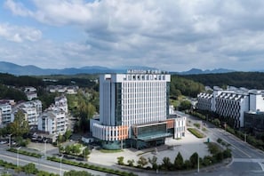 A modern hotel with a prominent central tower, surrounded by smaller buildings and a road. - Madison Hotel Huangshan Scenic Area North Gate (Huangshan City)