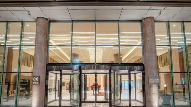 Fachada de hotel con puerta giratoria, amplios ventanales de vidrio y diseño interior moderno.