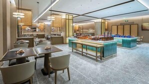 Un moderno vestíbulo de hotel con una zona de buffet central, arreglos de asientos e iluminación contemporánea.