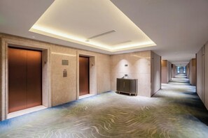Un couloir d’hôtel avec un tapis à motifs, un éclairage encastré et un comptoir de réception.