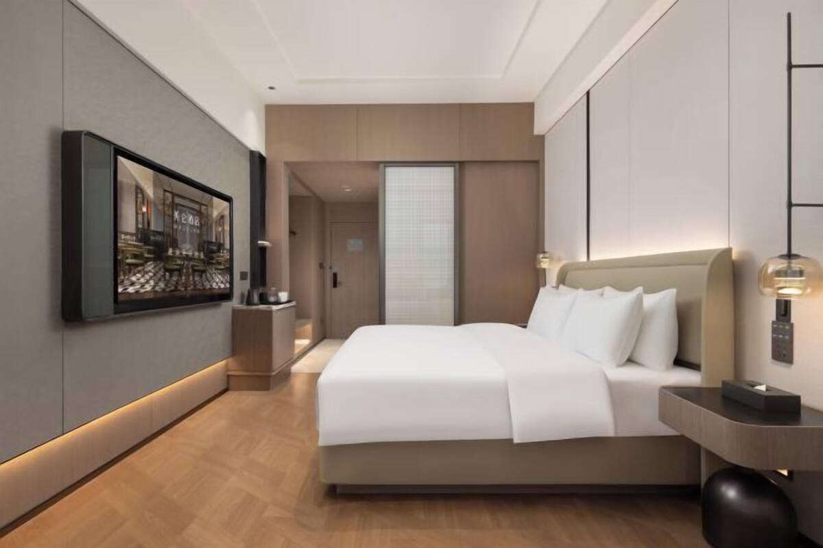 Ein modernes Hotelzimmer mit einem großen Bett, einem flachbildfernseher an der Wand und einem Nachttisch mit Lampe.