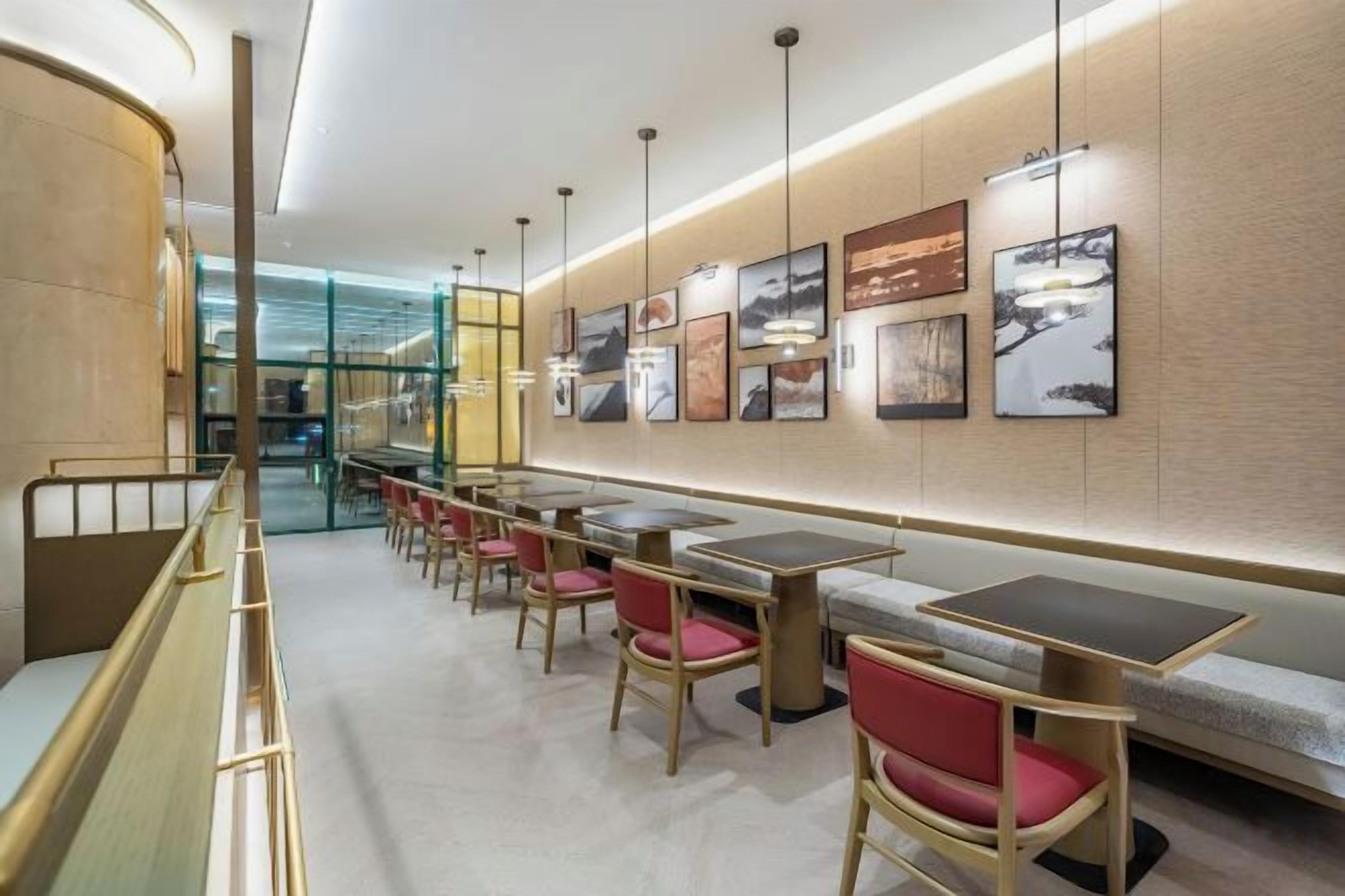 A modern restaurant with tables and chairs, a glass partition, and framed artwork on the walls.