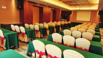 A conference room with rows of tables and chairs, a projector screen, and a stage.