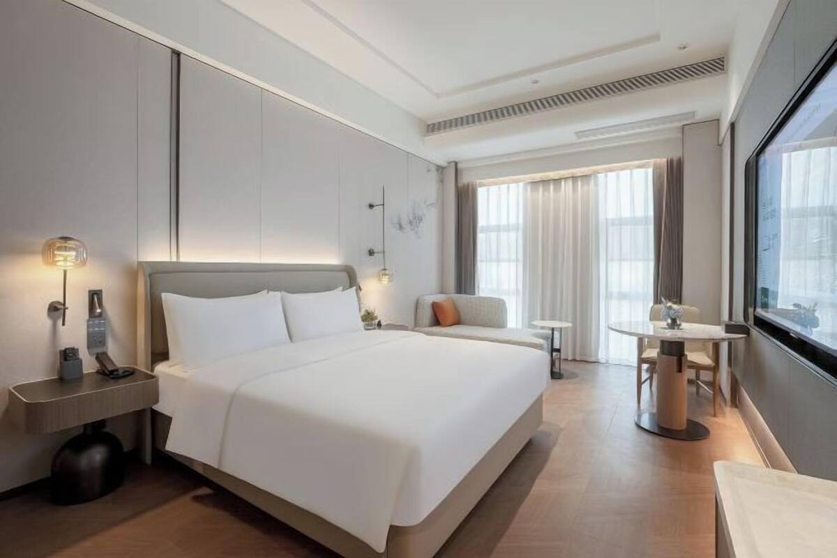 Ein Hotelzimmer mit einem großen Bett, Nachttischen, einem kleinen runden Tisch und einem Fenster mit Vorhängen.