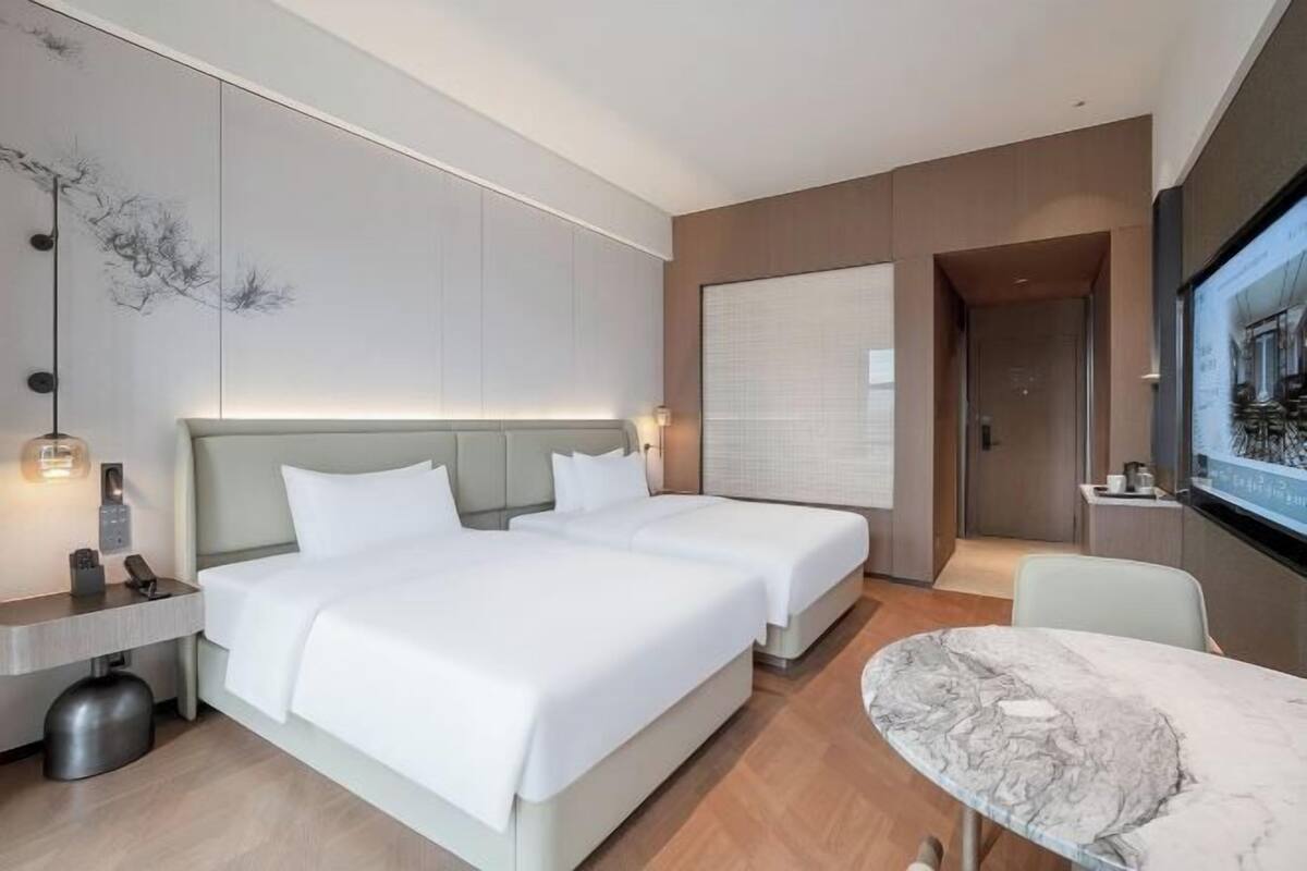 Ein modernes Hotelzimmer mit zwei Betten, einem Marmortisch und einem großen Fenster.