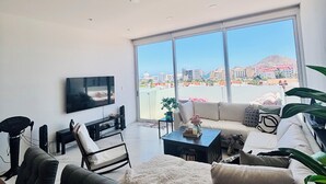 A modern living room with a large TV, comfortable seating, a coffee table, and a view of a cityscape through large windows.