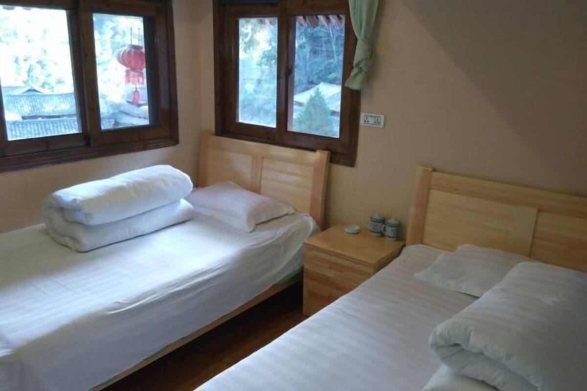 Ein Zimmer mit zwei Betten, einem Holzkopfstück, einem Nachttisch mit Lampe und einem Fenster mit Vorhängen.