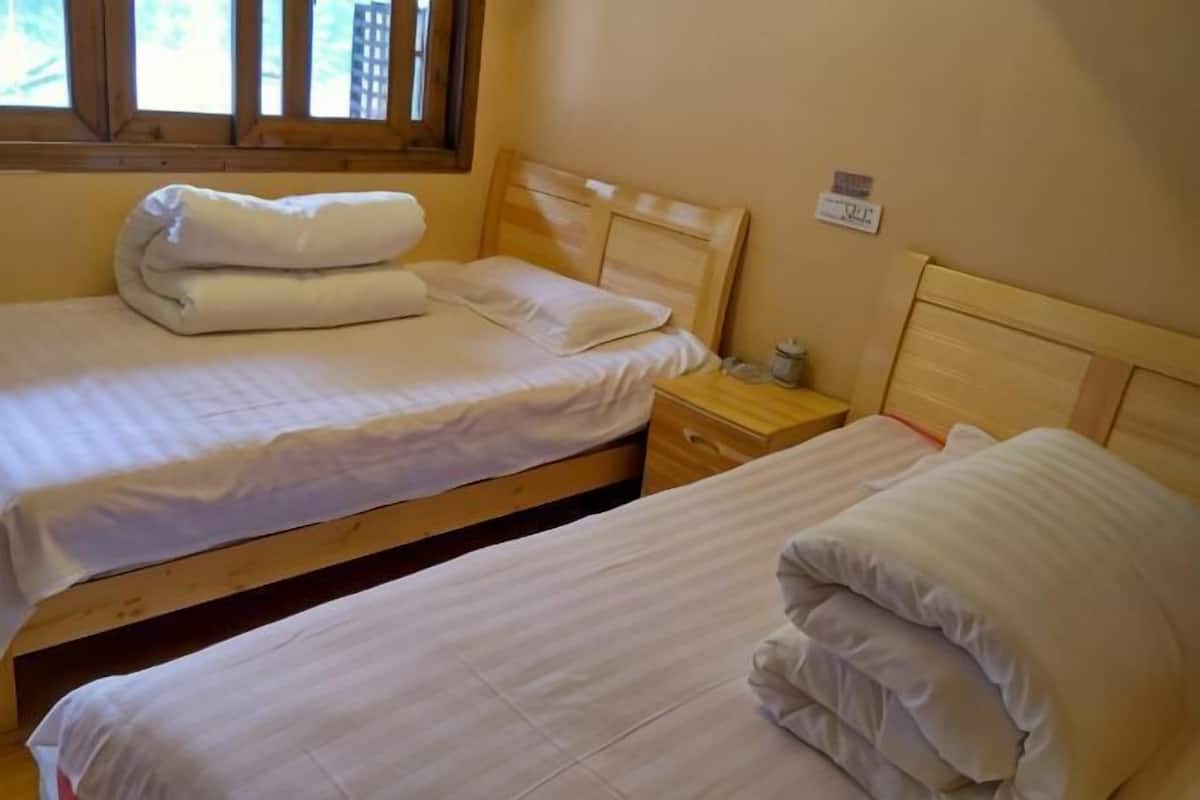 Una habitación con dos camas individuales, cabeceros de madera, una mesita de noche con lámpara y una ventana con persianas.