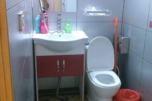 A bathroom with a white sink, red cabinets, a toilet, and a red trash bin.