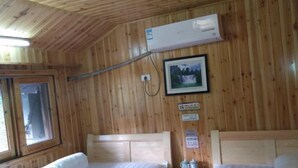 Habitació d'una cabana de fusta amb dos llits, un aparell d'aire condicionat, una finestra i un quadre al mur.