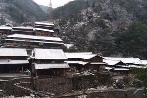 A traditional multi-story building with a series of connected structures, likely a hotel or guesthouse, set in a mountainous area with snow-covered roofs. - Yongjia Yongping Home Inn (Yongjia)