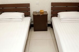 Una habitación de hotel con dos camas individuales, una mesita de noche de madera entre ellas y un almohadón blanco en cada cama.