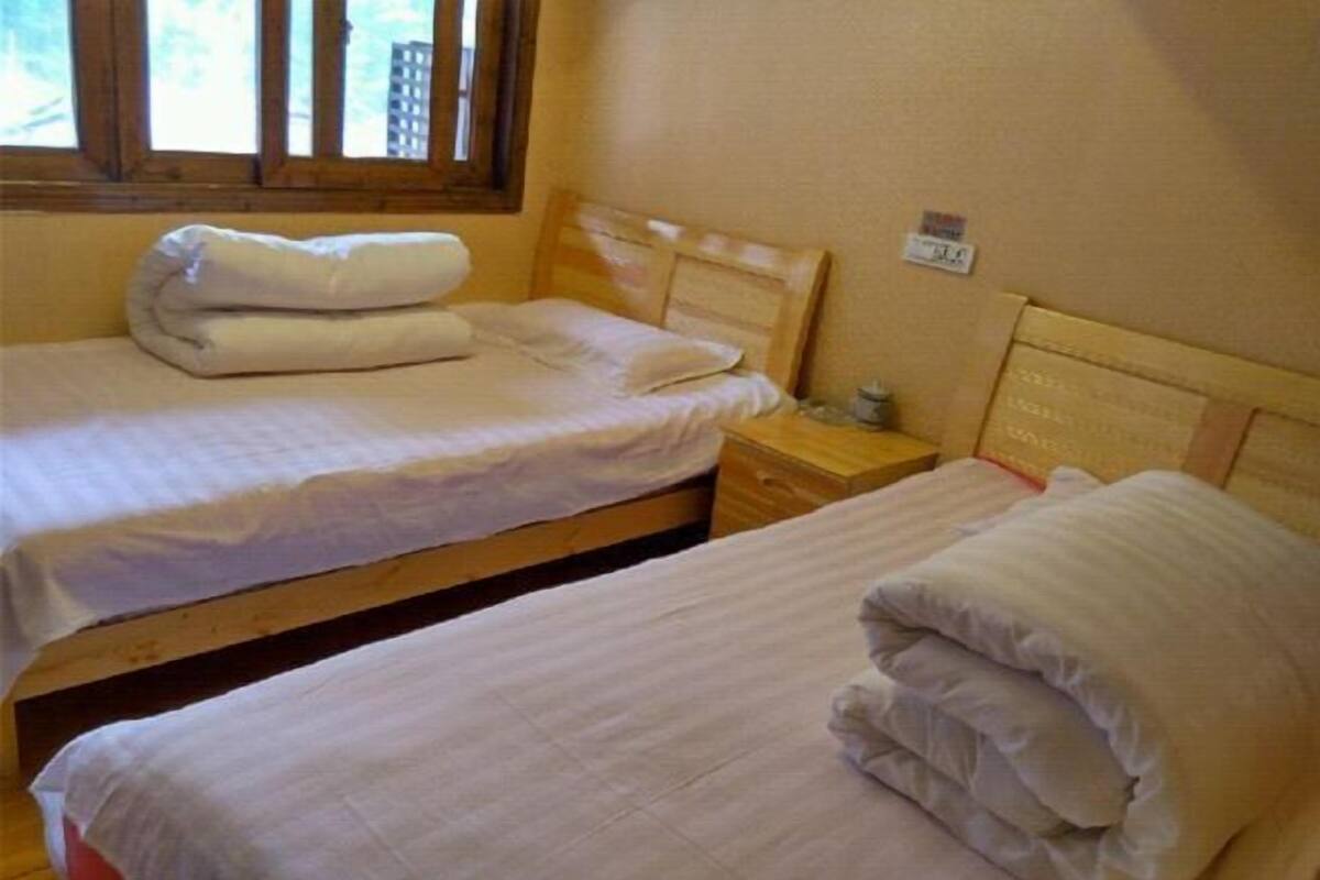 Ein Zimmer mit zwei Einzelbetten, Holz-Kopfteilen, einem Nachttisch mit Lampe und einem Fenster mit Jalousien.