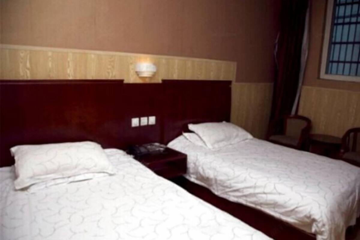 Ein Hotelzimmer mit zwei Einzelbetten, einem Holzkopfteil, einem Nachttisch und einem Fenster mit Gitterstäben.