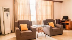 A modern hotel room with two sofas, a glass table, a TV, and a minibar. - Xing Qiang Hotel (Longmen)