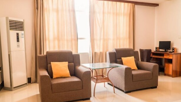 Quarto de hotel moderno com dois sofás, uma mesa de vidro, televisão e minibar.
