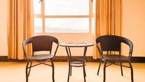 Duas cadeiras de vime e uma mesa redonda pequena num quarto com paredes bege e uma janela grande com cortinas.