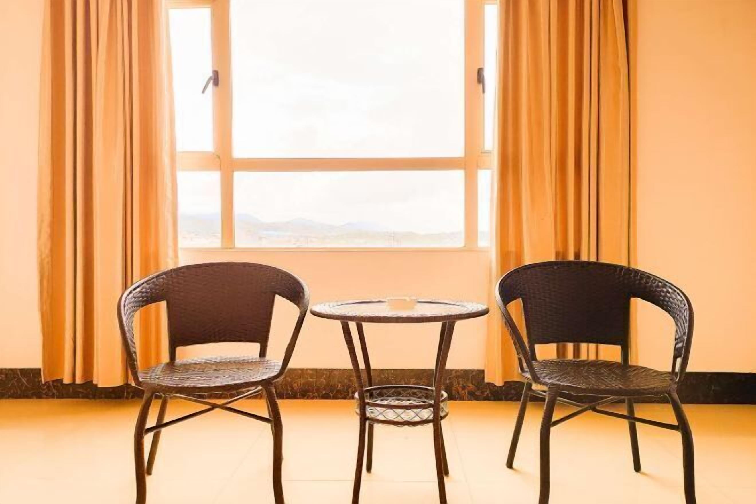 Dos sillas de mimbre y una pequeña mesa redonda en una habitación con un ventanal y cortinas.