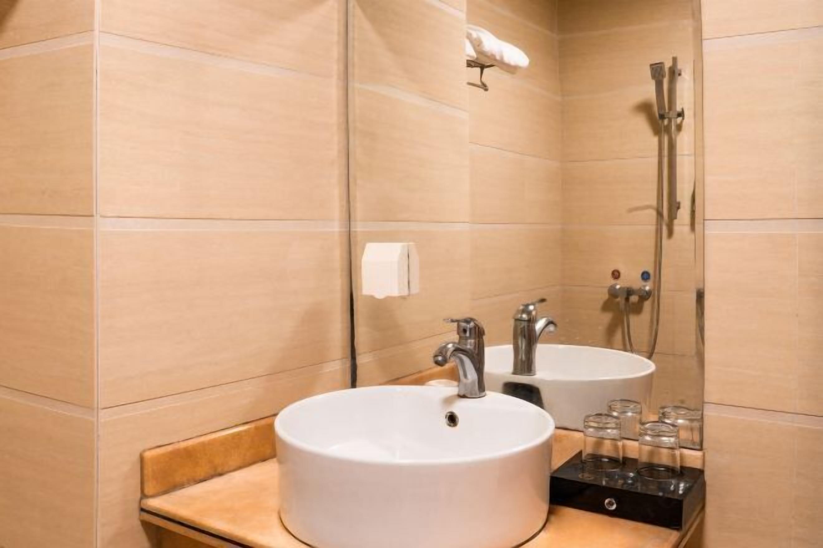 Un baño con un lavamanos blanco, dos grifos, un espejo y una ducha.