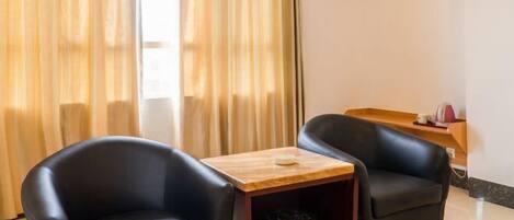 A room with two black leather chairs, a wooden side table, a trash bin, and a wall-mounted air conditioning unit.