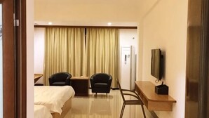 Quarto de hotel com uma cama, duas cadeiras, uma escrivaninha, uma televisão e uma cortina.