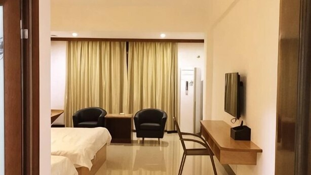 A hotel room with a bed, two chairs, a desk, a television, and a curtain. - Xing Qiang Hotel (Longmen)