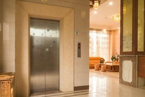 An elevator with a metallic finish and decorative snowflake patterns, a reception area with a sofa and coffee table, and a well-lit interior. - Xing Qiang Hotel (Longmen)