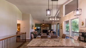 A spacious kitchen with a large island, pendant lighting, and a stone fireplace. - Fairway Gem at Spruce Pine - EV charge port, hot tub, fishing access (Spruce Pine)