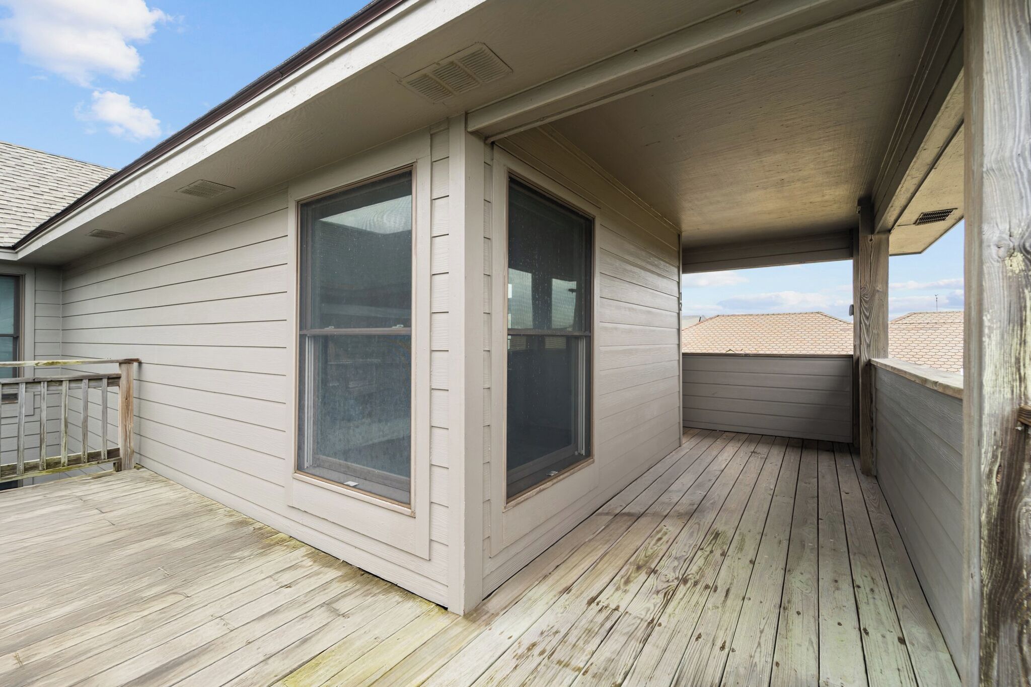 A covered balcony with wooden flooring and large windows.