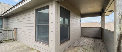 A covered balcony with wooden flooring and large windows.