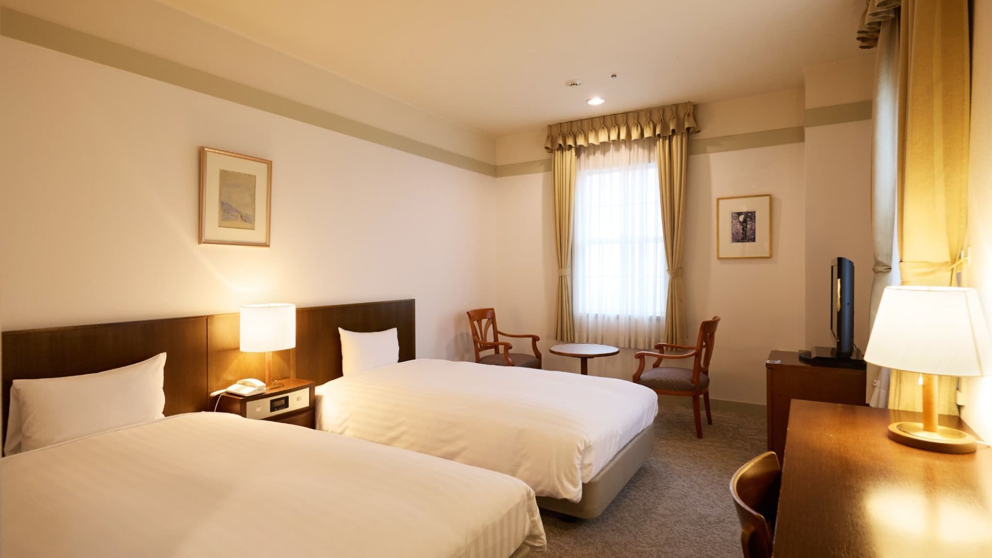 Ein Hotelzimmer mit zwei Betten, einem Schreibtisch, einem Stuhl, einem kleinen Tisch und einem Fernseher.